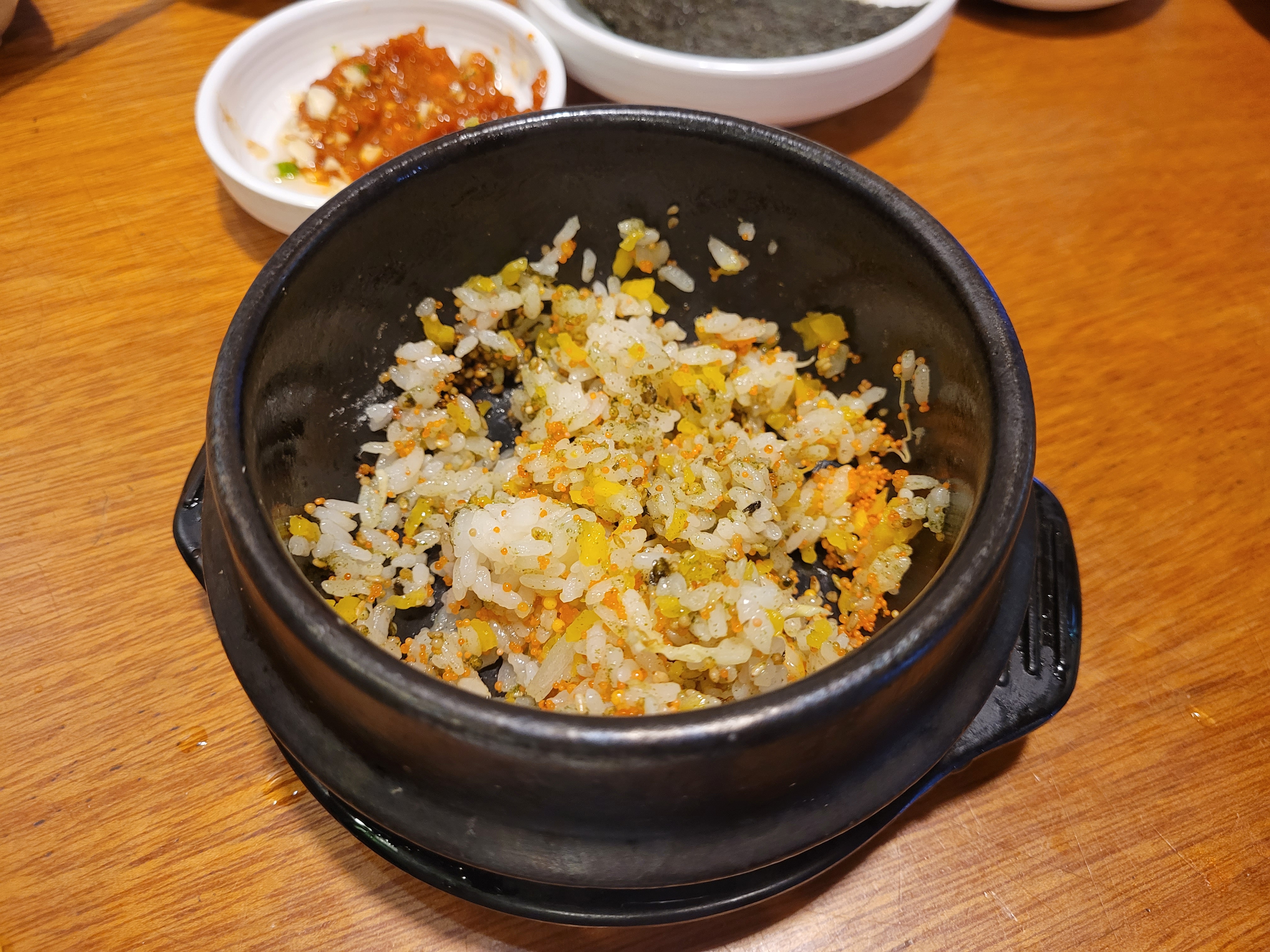 검은 돌솥 속 날치알 볶음밥, 노란 단무지, 초록 플레이크