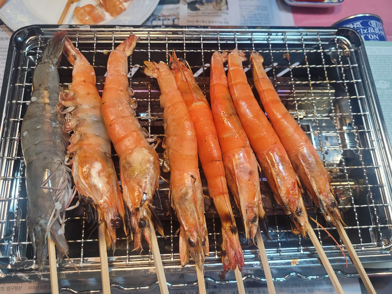 석쇠 위, 익어가는 주황색 새우 꼬치와 회색 생새우