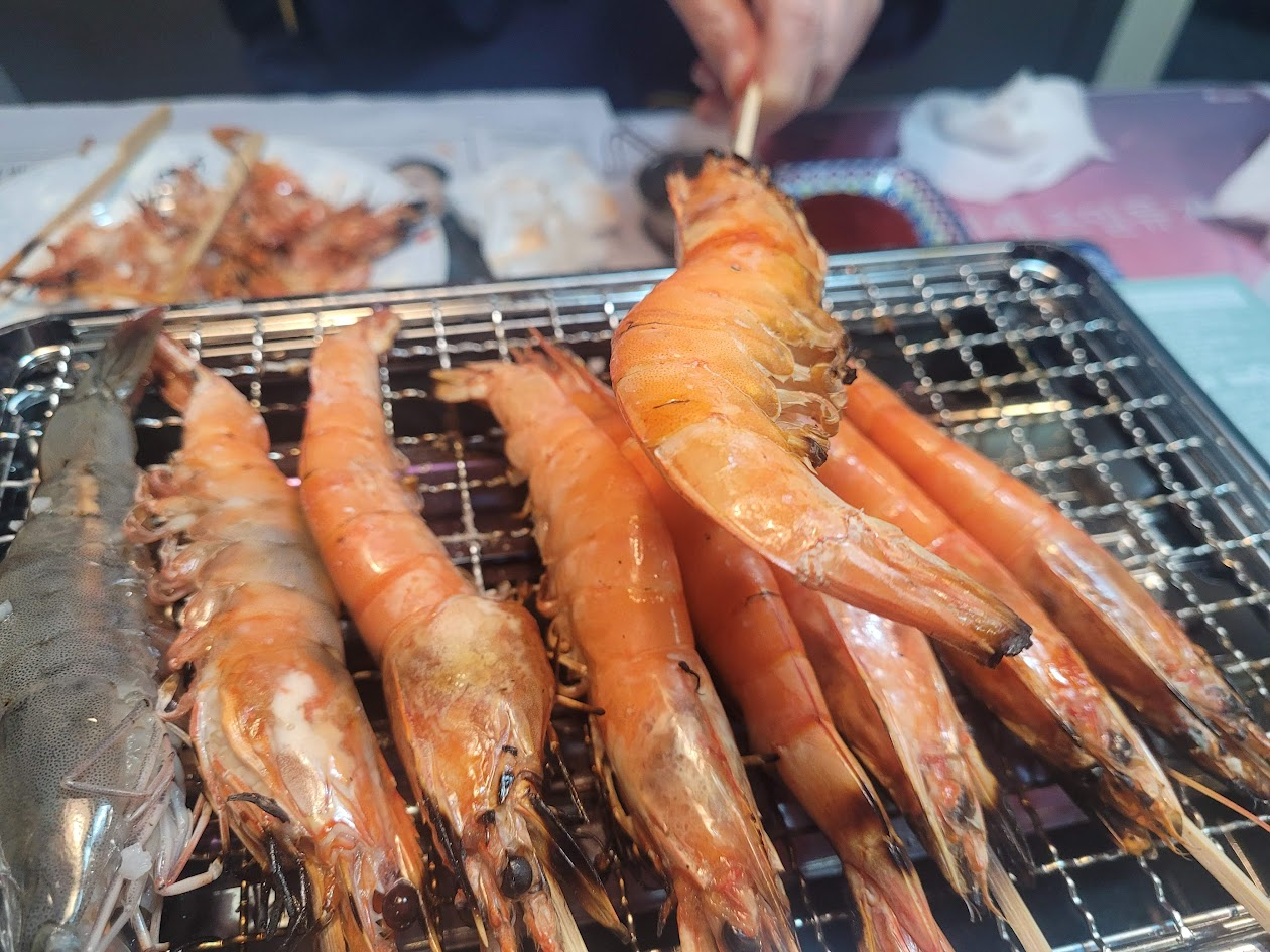 석쇠 위 큼직한 새우, 꼬치에 꿰어 익어가는 해산물 구이