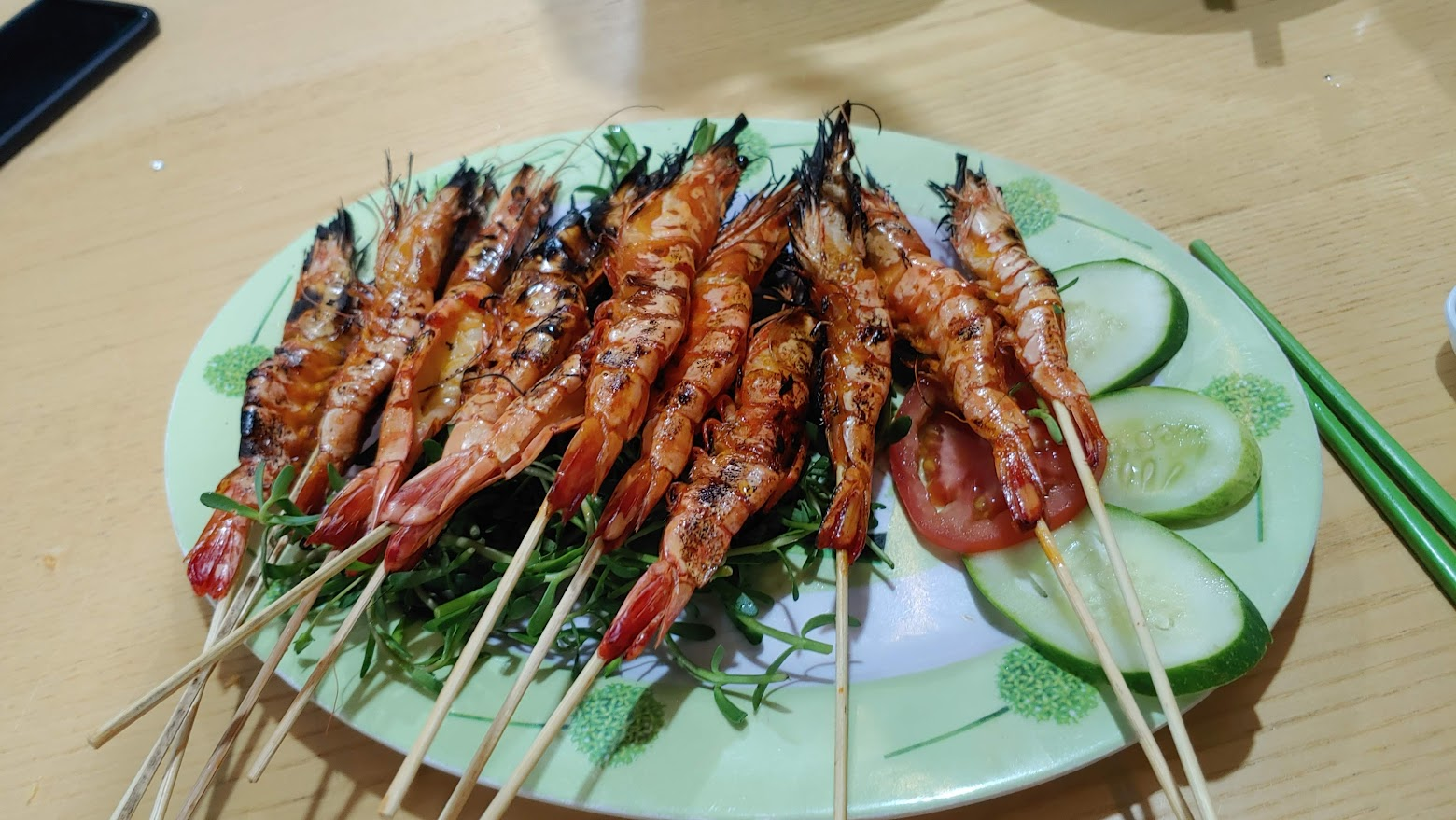 녹색 접시에 놓인 구운 새우 꼬치, 오이, 토마토, 잎채소