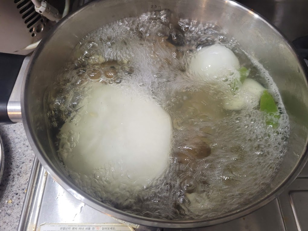 끓는 물 냄비 안 양파, 채소, 버섯 조리 중