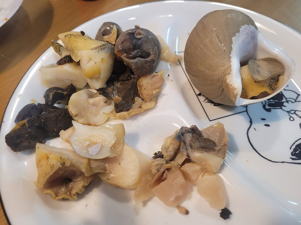 흰 접시 위 삶은 골뱅이와 껍데기, 먹음직스러운 해산물 요리.