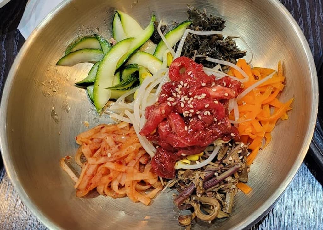 스테인리스 그릇에 담긴 육회, 호박, 당근, 콩나물 비빔밥
