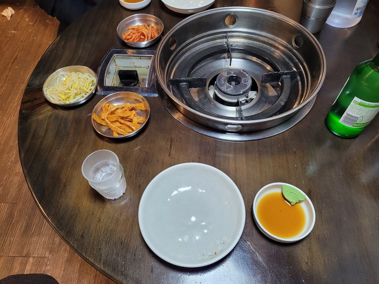 갈색 나무 탁자 위 불판, 반찬, 소주병, 소주잔