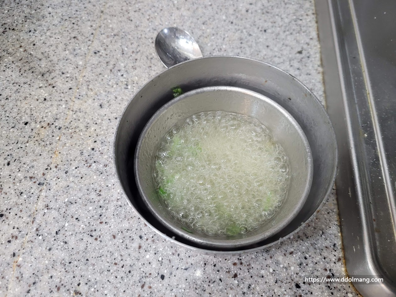 금속 그릇 안 끓는 국물, 녹색 채소 조각들