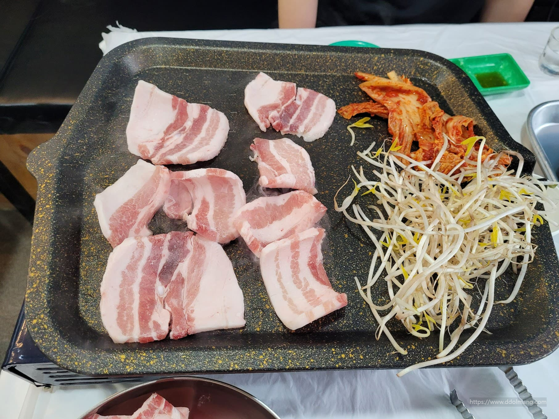 불판 위 두툼한 생삼겹살, 김치, 콩나물 구이