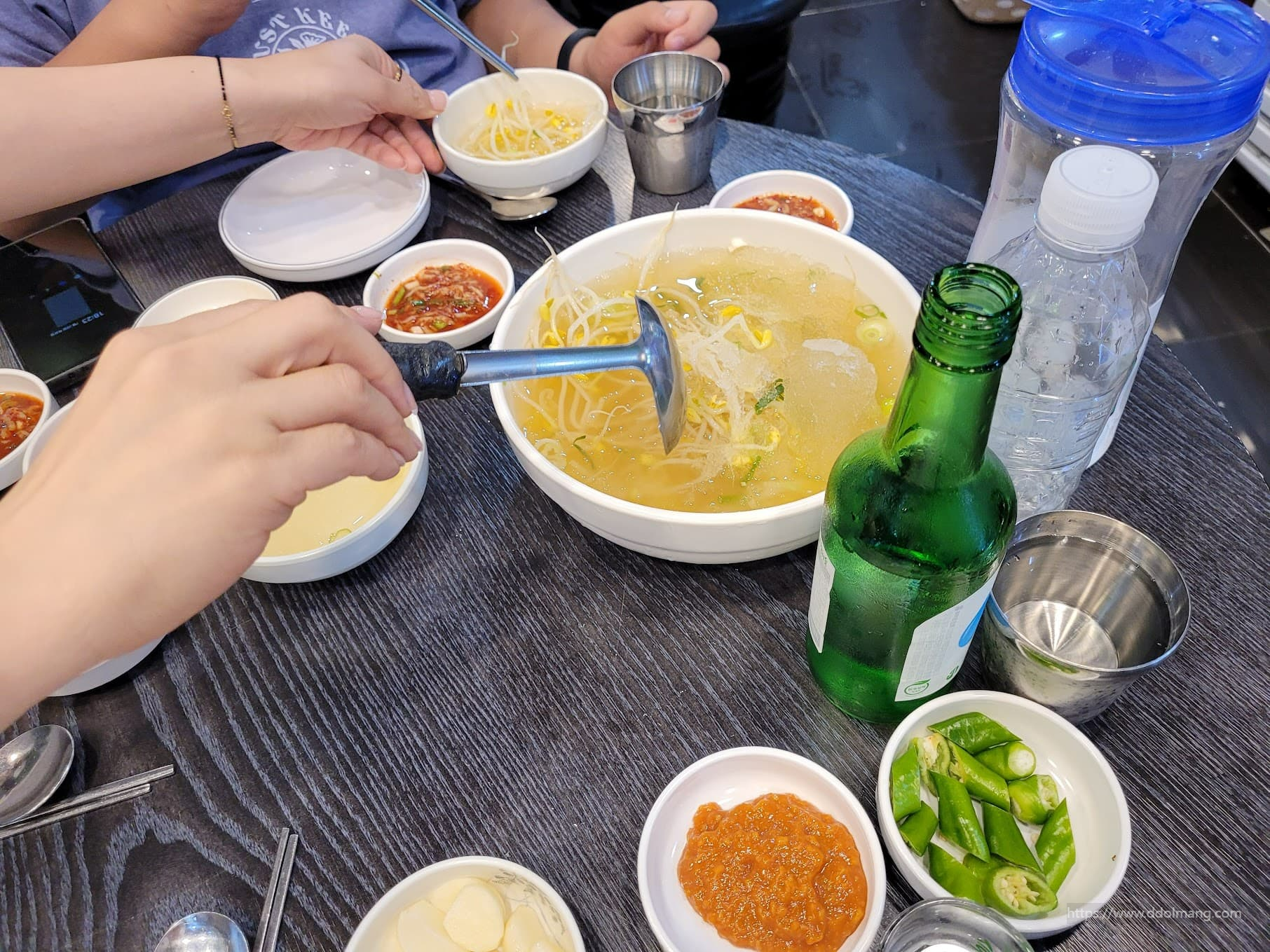 시원한 얼음 콩나물국, 소주, 한식 반찬 가득한 식탁.