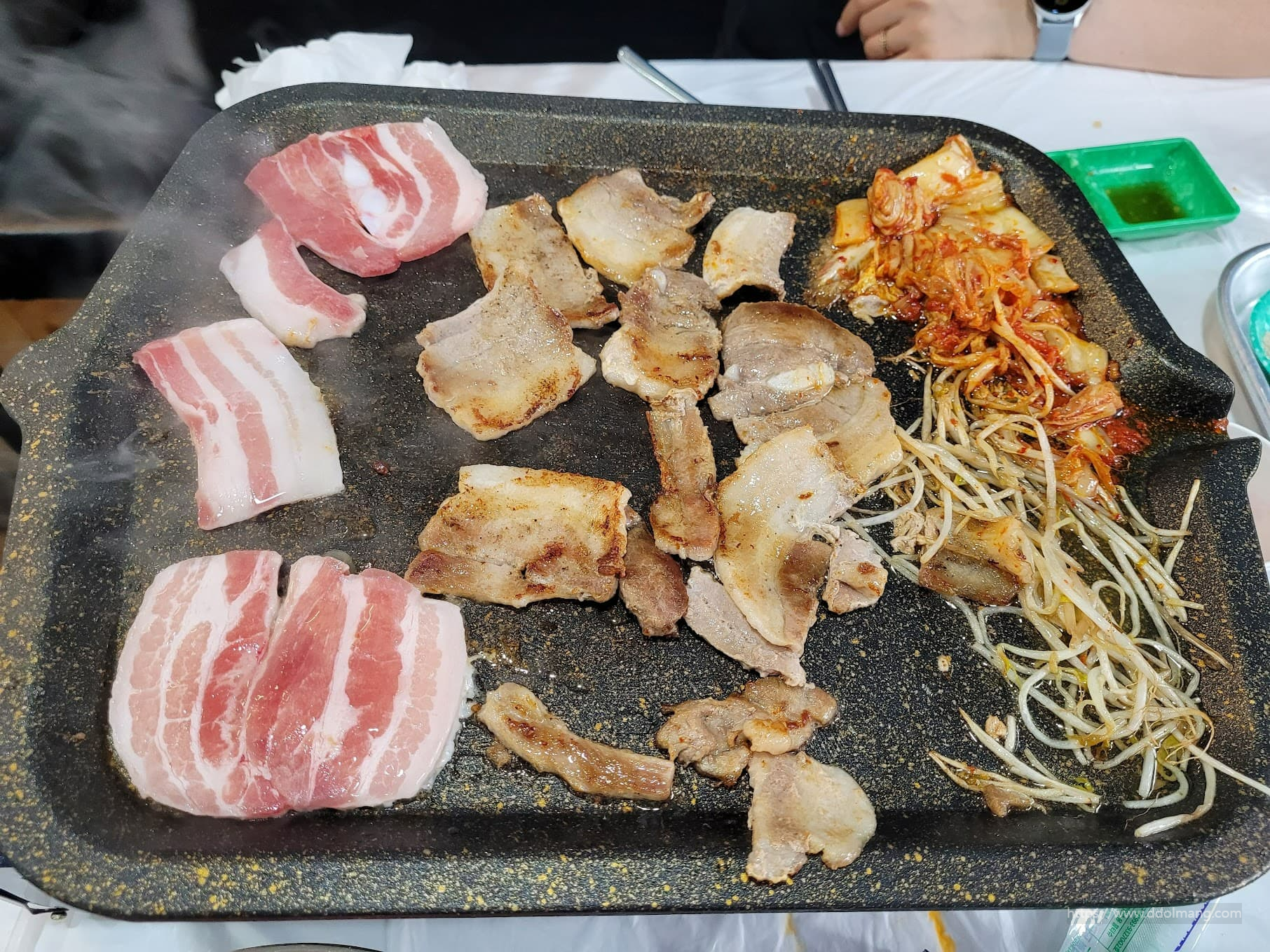 지글거리는 불판 위 삼겹살, 김치, 콩나물, 익어가는 돼지고기