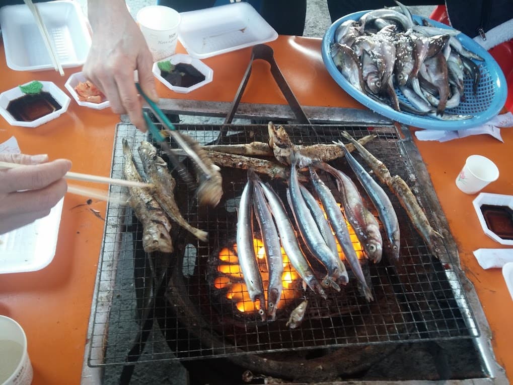 손으로 숯불 석쇠 위 작은 생선 구이 조리