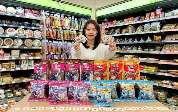 편의점 진열대 앞, 트레이딩 카드 든 미소 짓는 얼굴, 과자 봉지