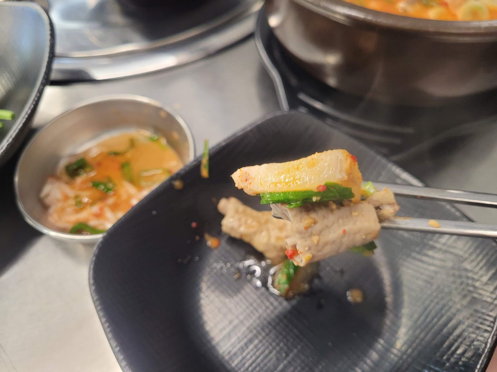 젓가락으로 집은 삼겹살 김치쌈, 소스와 찌개 배경.
