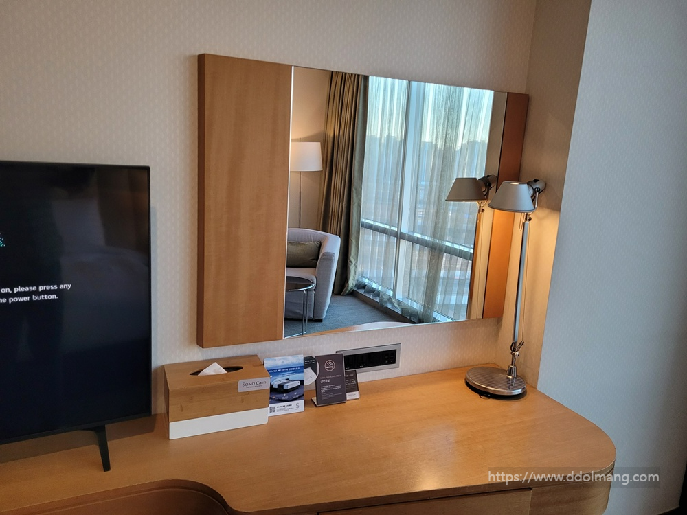 우드 데스크, 거울, 스탠드 조명, TV. 거울에 객실 창문 반사.