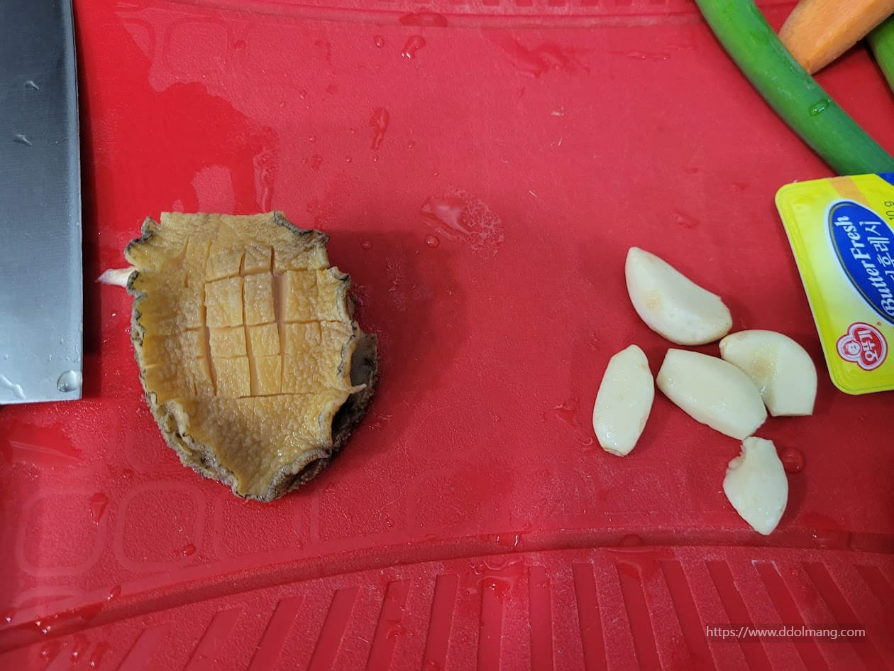빨간 도마 위 칼집 낸 전복, 마늘, 버터 준비