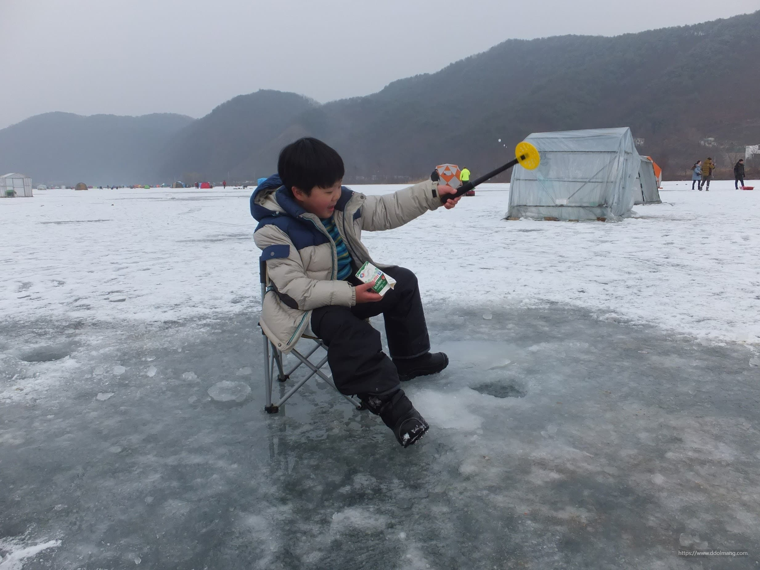 겨울 얼음 호수, 낚시 의자 앉아 낚싯대 들고 미끼 확인.