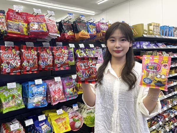 미소 짓는 이가 편의점 젤리 진열대에서 두 가지 제품을 든다.