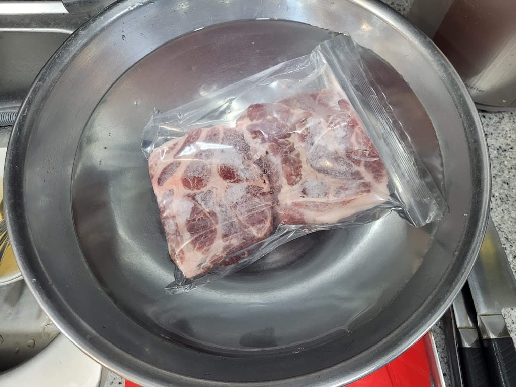 진공 포장된 생 돼지고기, 스테인리스 그릇 물에 해동 중