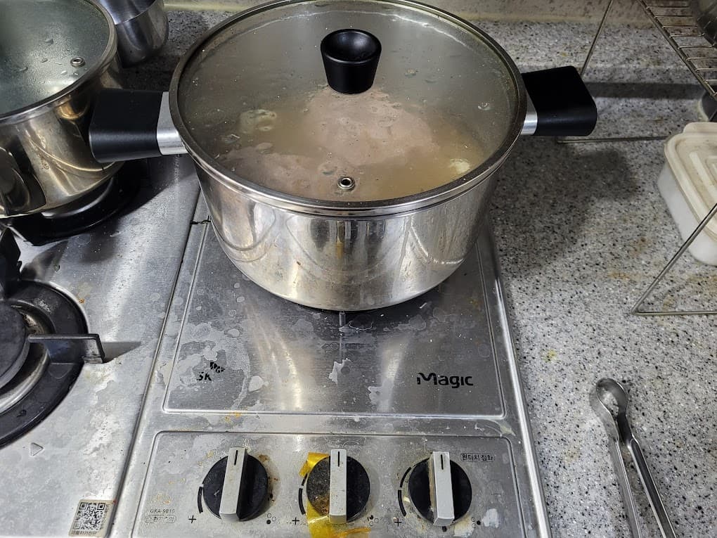 끓는 중인 스테인리스 냄비, 지저분한 매직 가스레인지, 주방 카운터.