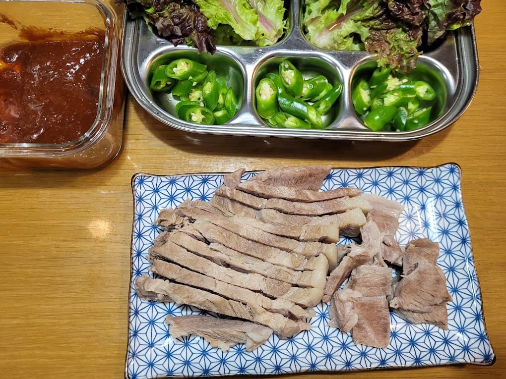 수육, 쌈장, 썰린 청고추, 신선한 상추 곁들인 한식 차림