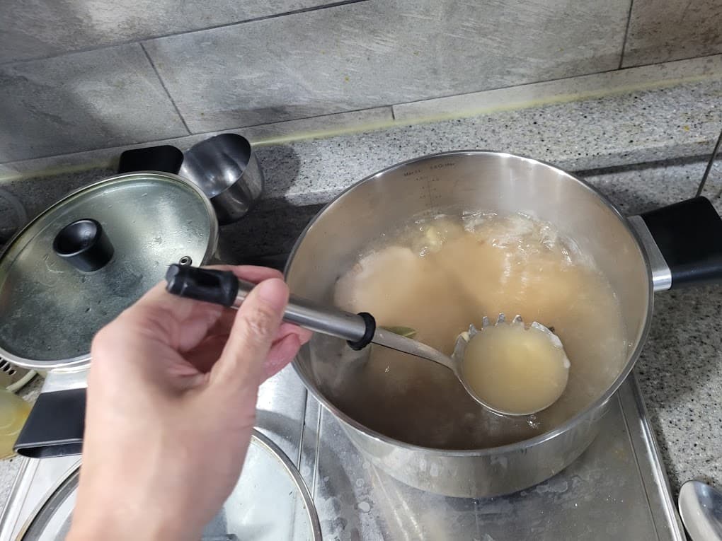국자로 끓는 육수 냄비에서 거품 걷는 동작