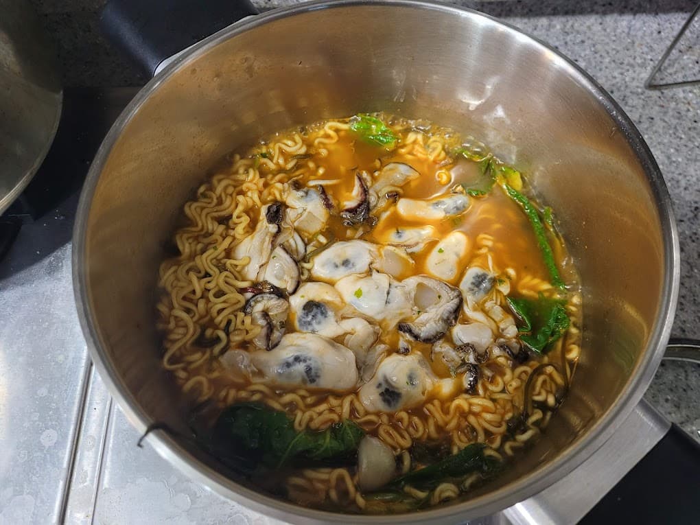 냄비 굴 라면 면발 녹색 채소 빨간 국물