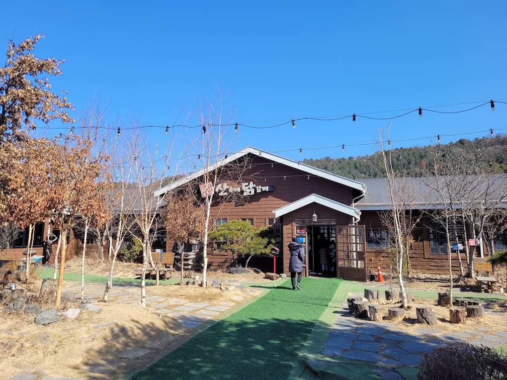 산골닭갈비 목재 건물, 마른 나무, 녹색 진입로, 푸른 하늘.