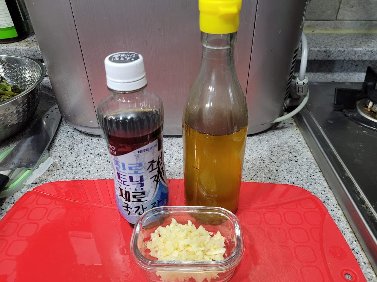 주방 조리대 빨간 도마 위 국간장, 참기름, 다진 마늘 재료