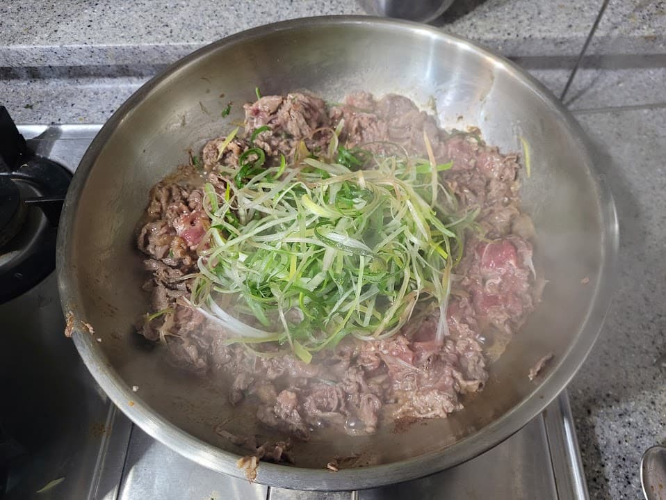 지글거리는 양념 소고기 불고기, 파채 함께 팬에서 조리 중