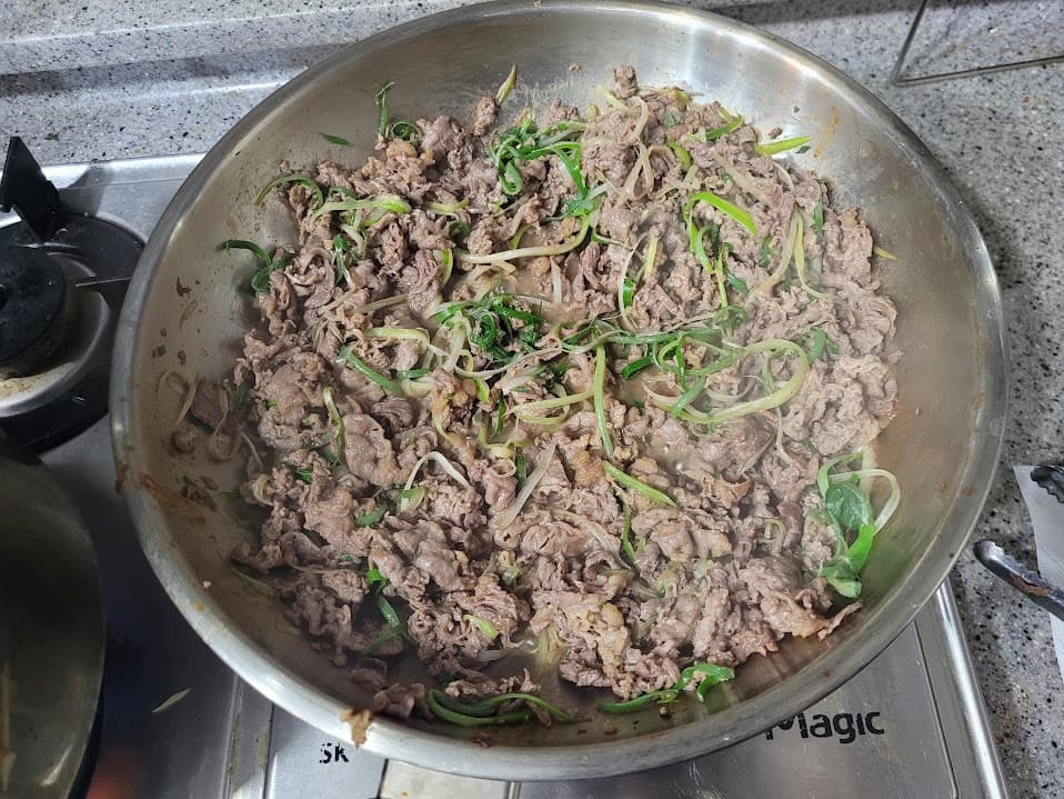 스토브 위 팬에서 지글거리는 소고기 파채 볶음 요리