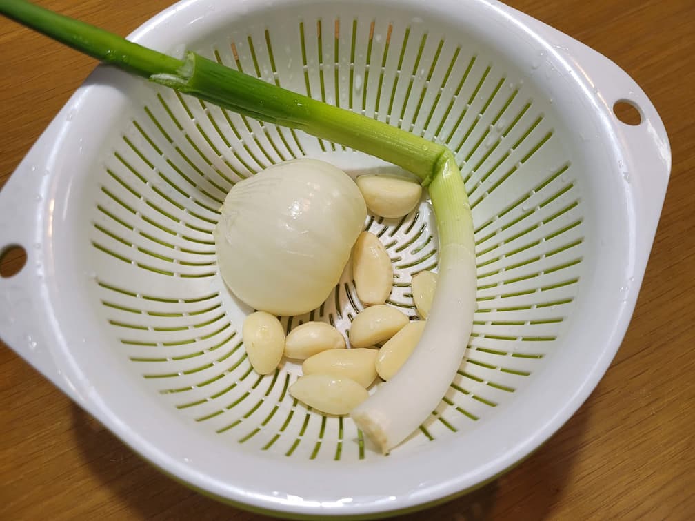 하얀 채반 안 신선한 껍질 벗긴 양파, 마늘쪽, 대파