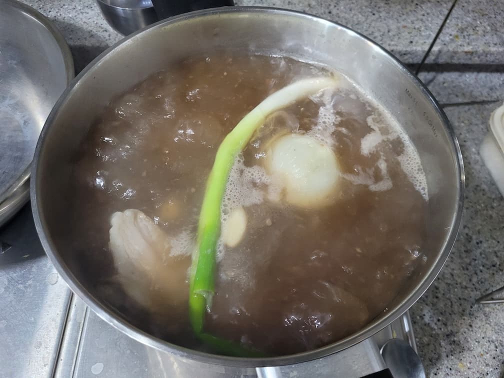 끓는 냄비 속 고기, 파, 양파 육수 조리 중
