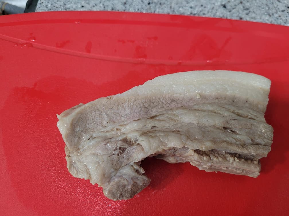빨간 도마 위 삶은 삼겹살 조각, 지방층과 살코기 선명.