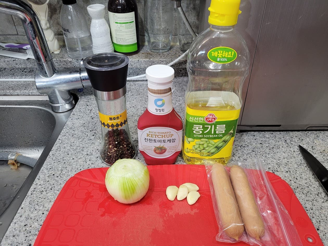 빨간 도마 위 양파, 마늘, 소시지, 케첩, 식용유, 후추.