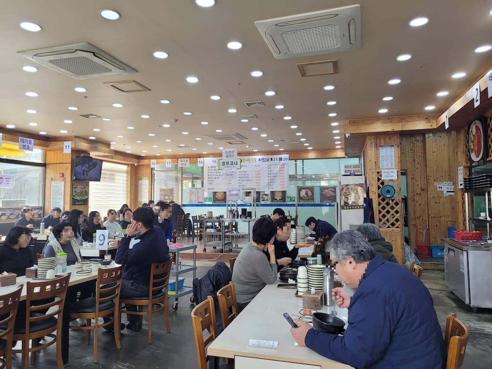 번화한 식당 내부, 많은 손님들 식사, 따뜻한 목재 장식, 밝은 조명