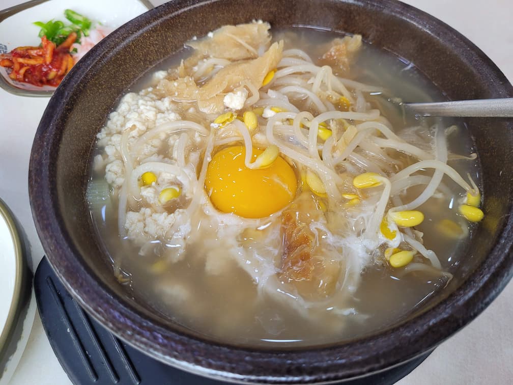 따뜻한 뚝배기 콩나물국, 날달걀 노른자, 순두부, 매콤한 반찬.