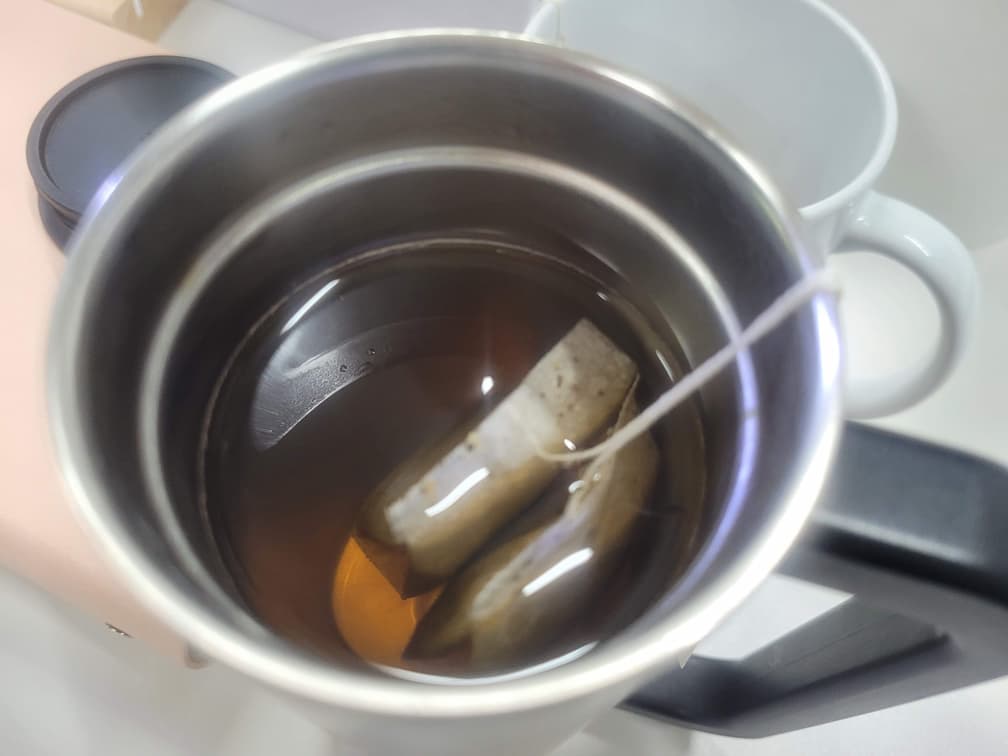 따뜻한 차 우림, 잠긴 티백 두 개, 금속 텀블러, 흰색 머그