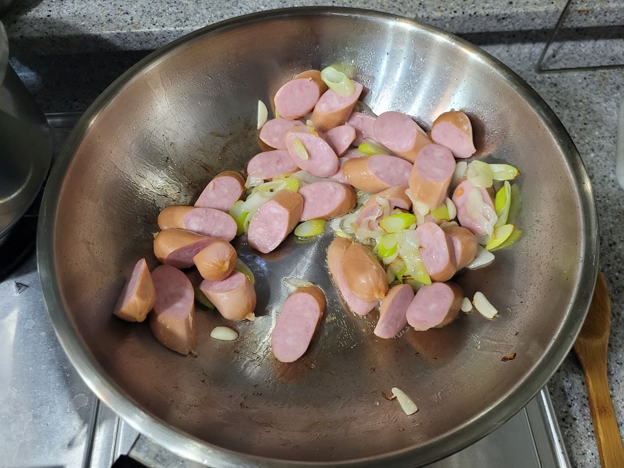 잘린 소시지, 대파, 마늘 스테인리스 프라이팬에서 볶는 중