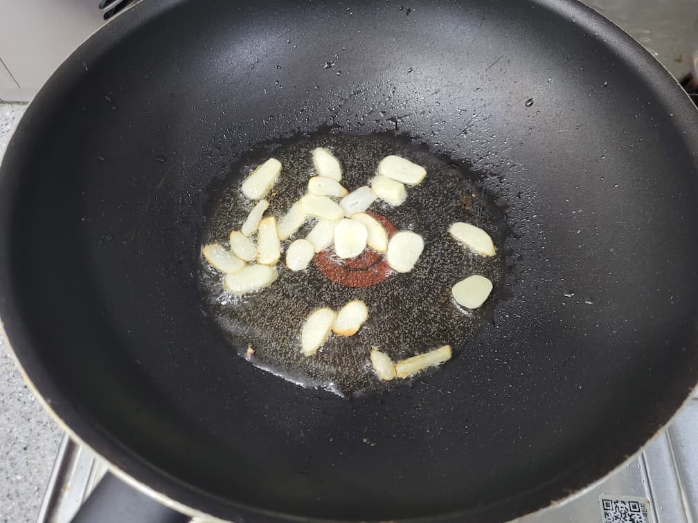 검은 프라이팬에서 끓는 식용유에 노릇하게 볶는 얇게 썬 마늘