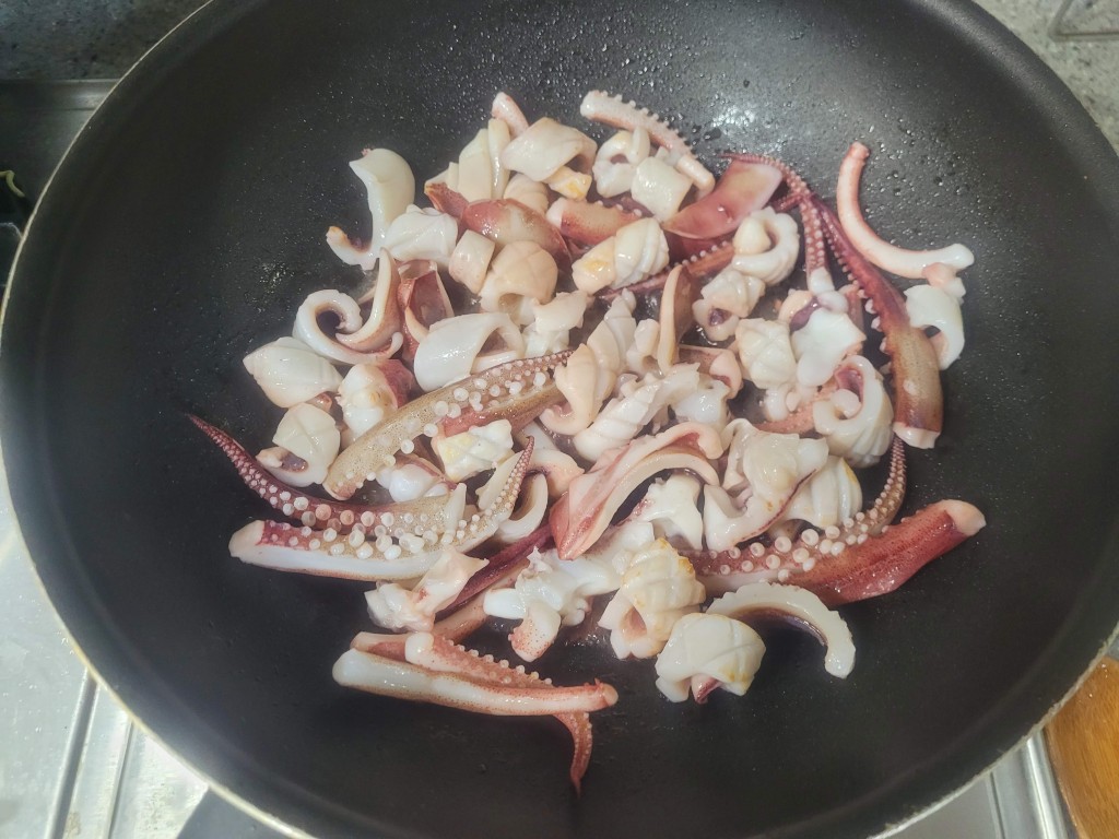 썰린 오징어 몸통과 다리 검은 프라이팬에서 조리 중