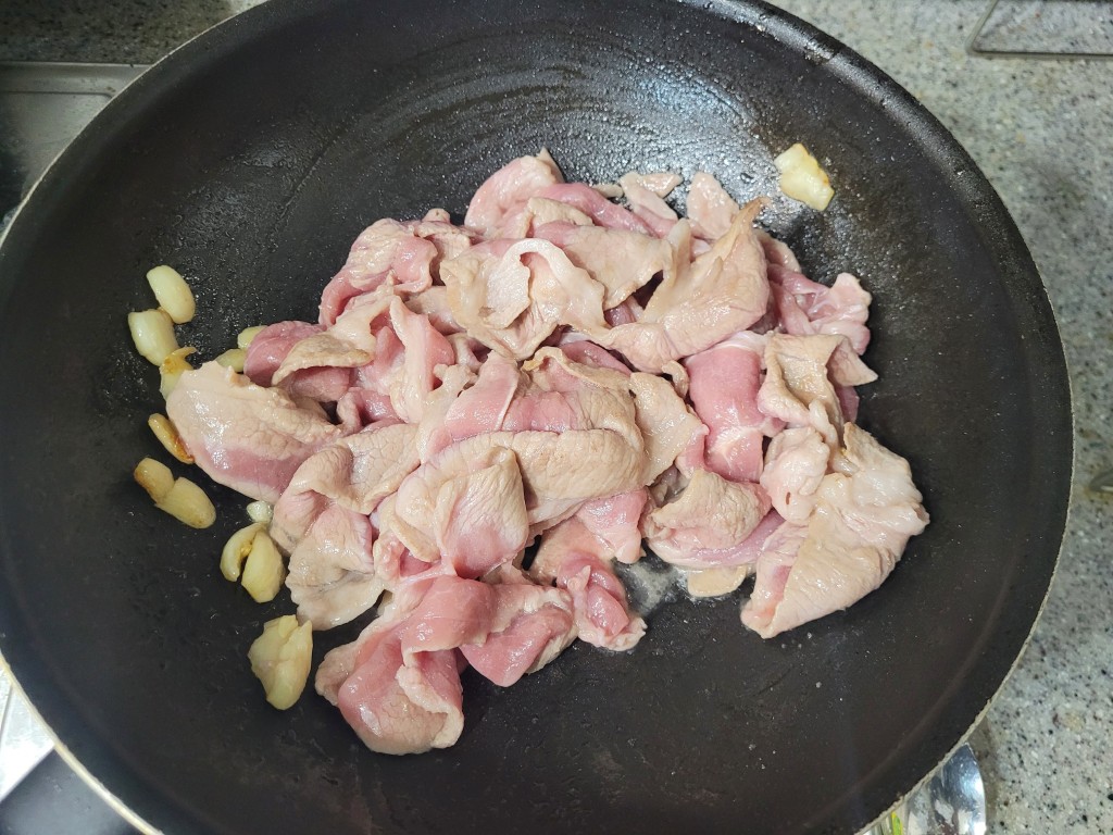 검은 팬 안 얇게 썬 신선한 돼지고기 슬라이스, 통마늘 조리