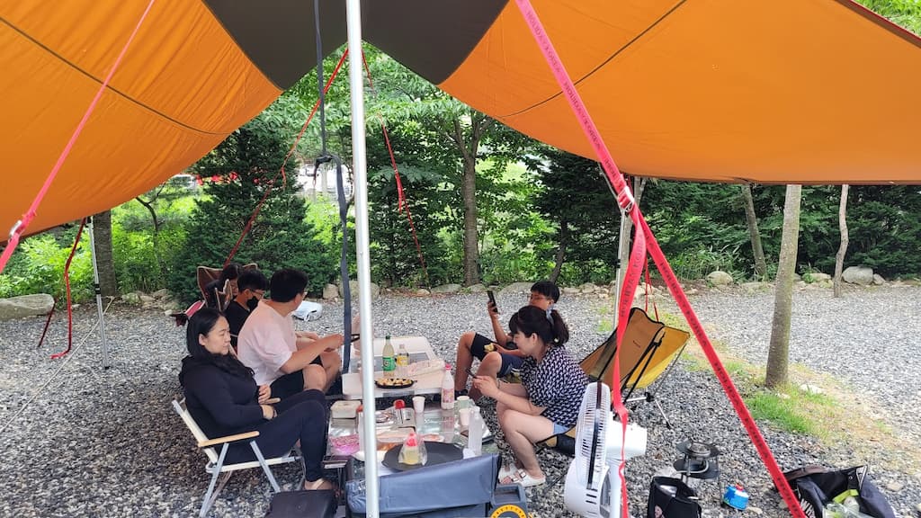 타프 아래 캠핑 테이블 주변에 모여 식사하는 일행