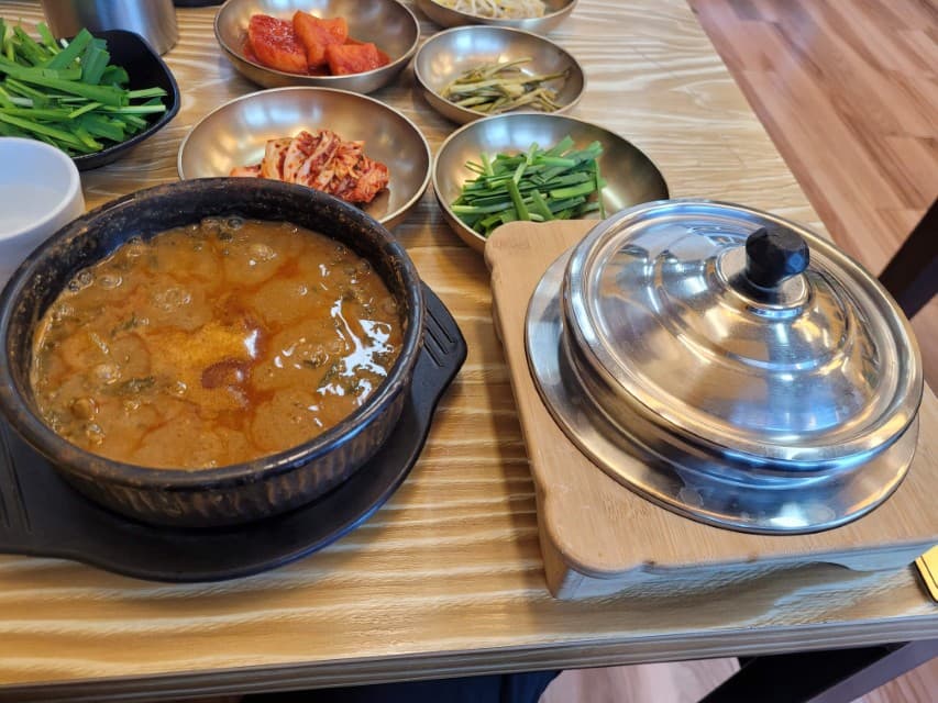 끓는 돌솥 청국장찌개, 은색 솥밥, 푸짐한 한정식 반찬 상차림.