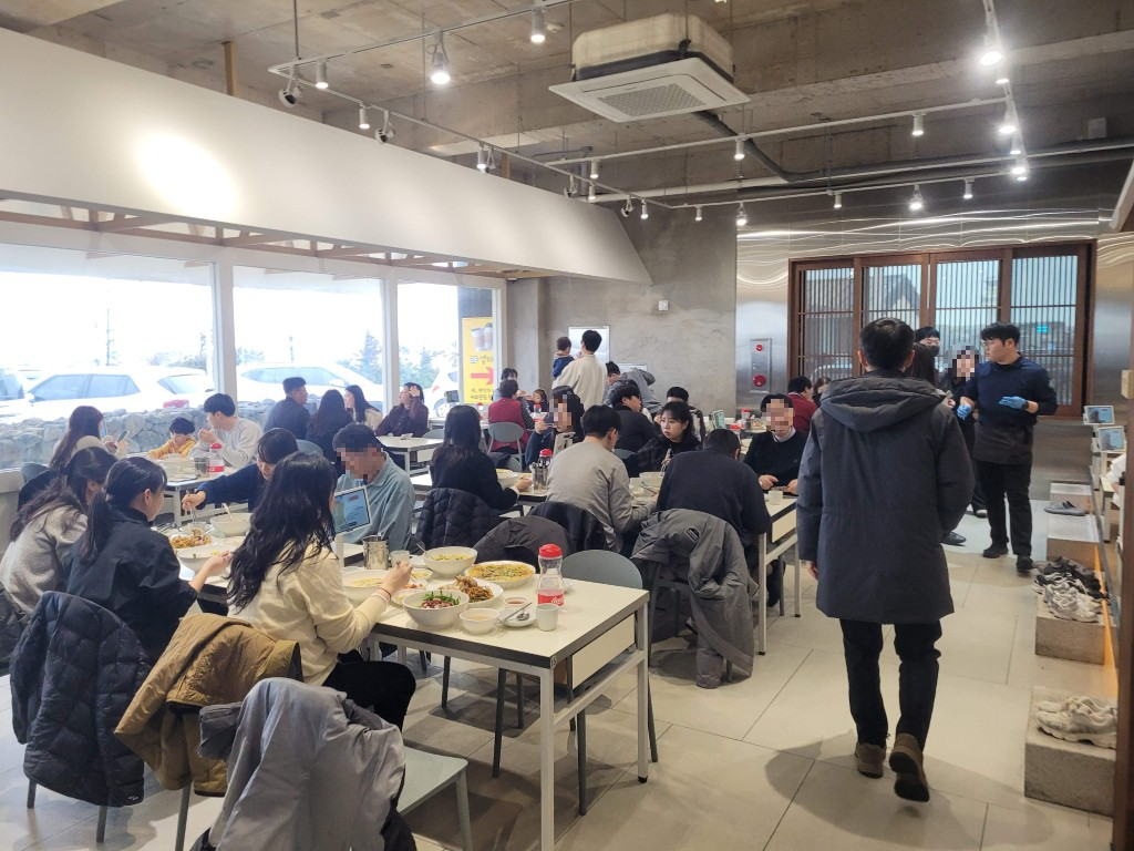 붐비는 현대적 식당, 많은 손님들이 식탁에서 음식 즐기는 중.