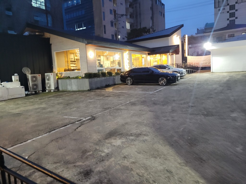 현대적 건물, 주차된 차량 두 대, 밤거리, 밝은 실내.