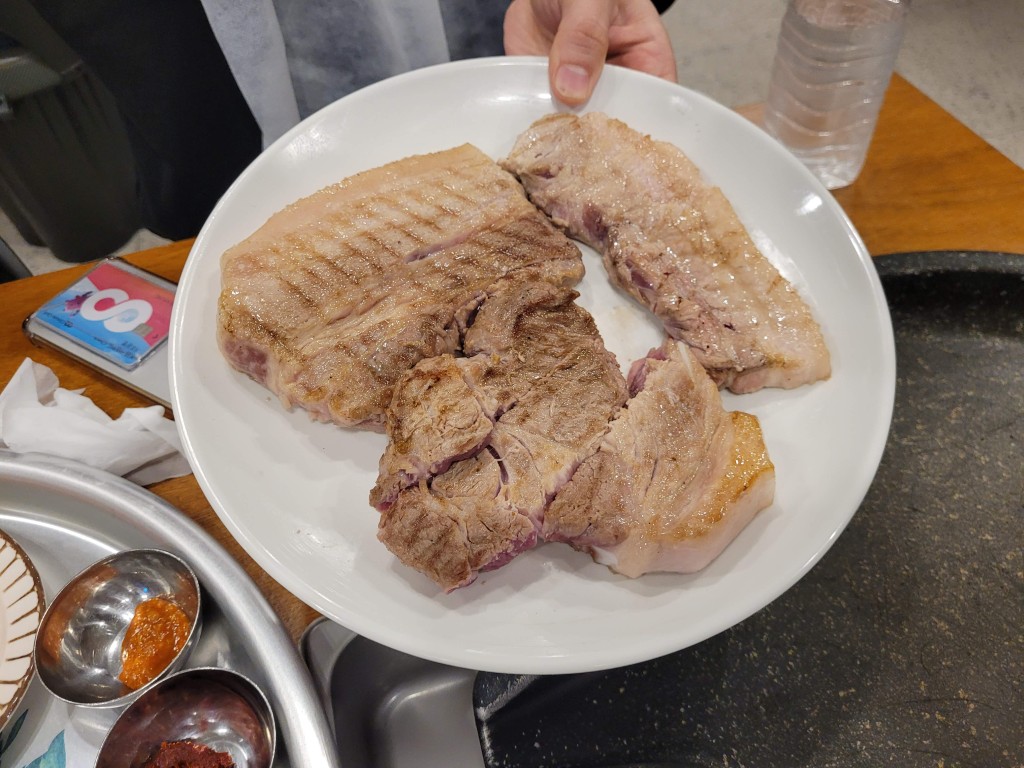 흰 접시 위 노릇하게 잘 구워진 두툼한 돼지고기 여러 점