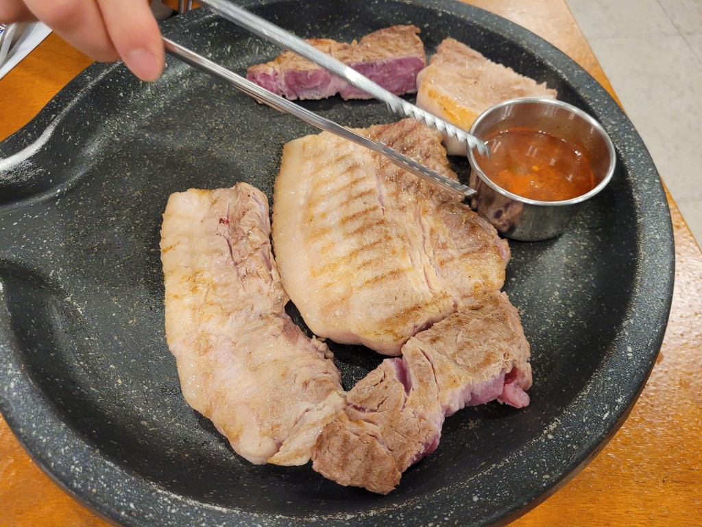집게로 굽는 두툼한 돼지고기, 돌판 위 매콤한 소스
