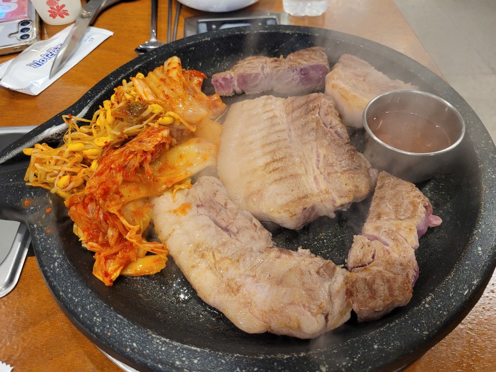 지글지글 뜨거운 돌판 위 노릇하게 익어가는 삼겹살, 김치, 콩나물