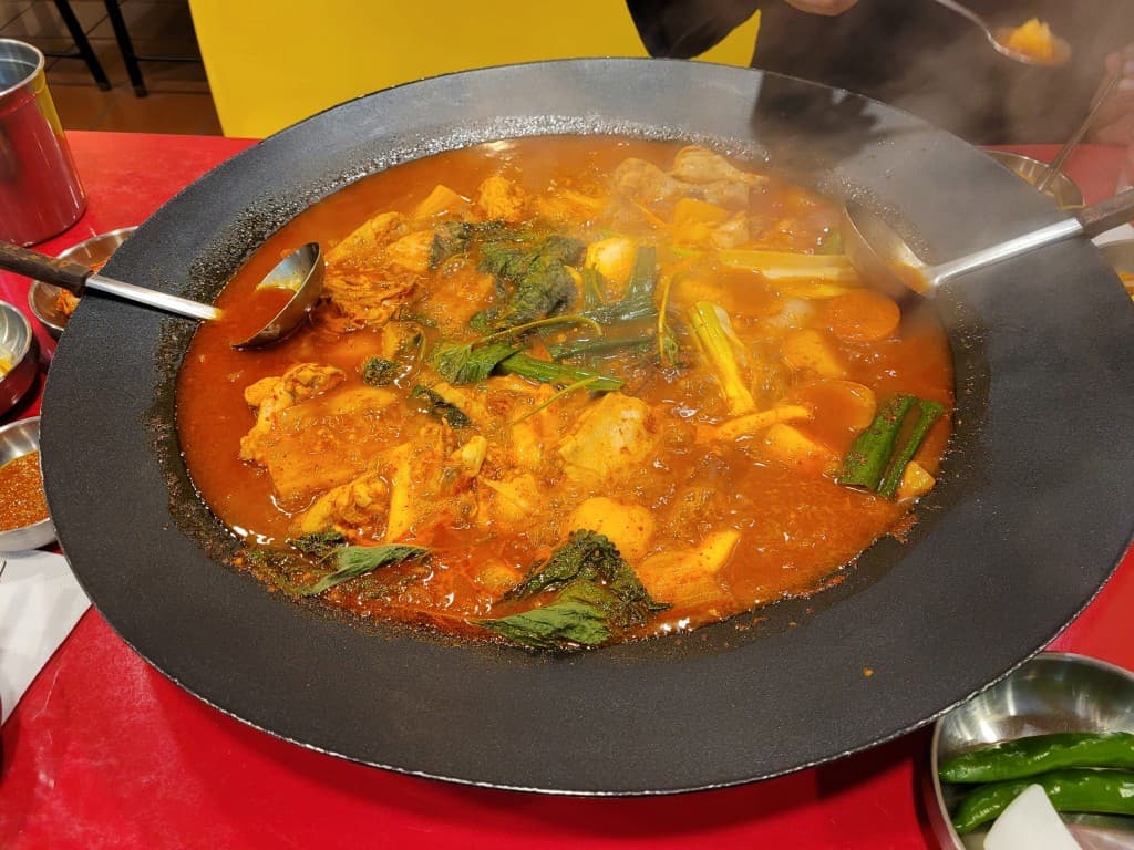 뜨거운 철판, 보글거리는 매콤한 닭갈비, 신선한 채소, 국자.