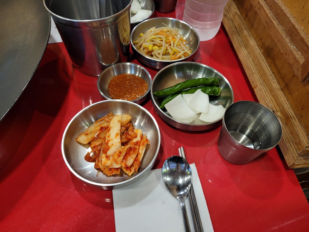 빨간 식탁 위 김치, 콩나물, 고추, 무 금속 그릇 반찬