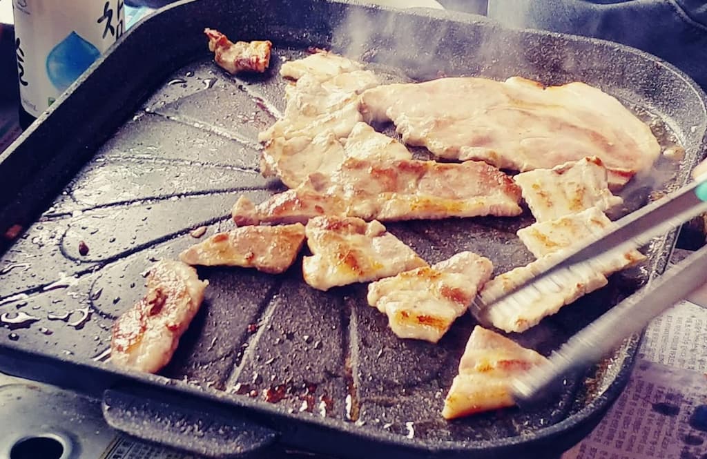뜨거운 불판 위 지글지글 굽는 두툼한 삼겹살, 집게, 소주병