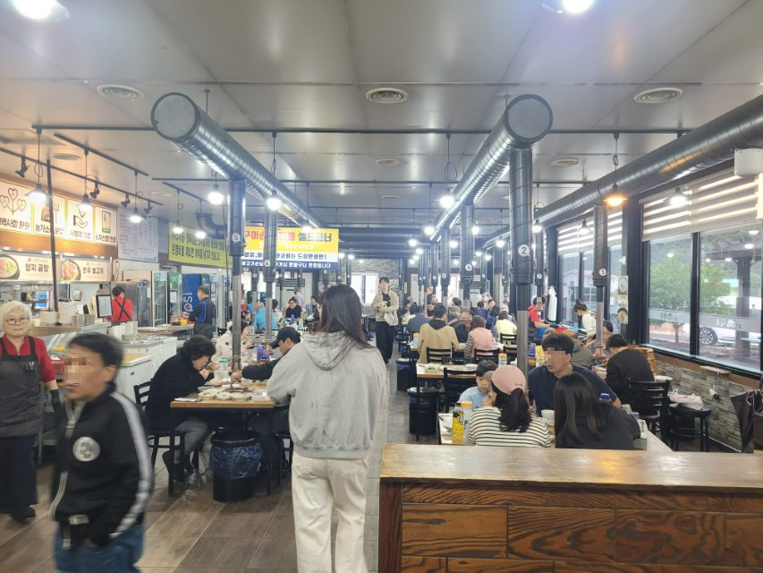 북적이는 한국 바비큐 식당 내부, 손님들 고기 구우며 식사.
